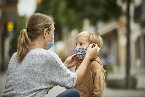 Mujer poniéndole una mascarilla a un niño para protegerlo del COVID-19