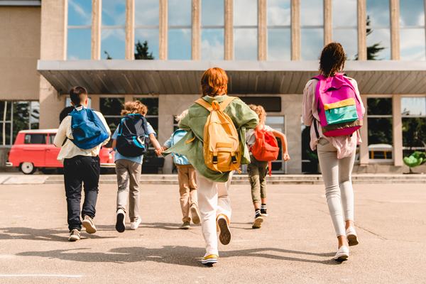 Niños pequeños, en edad escolar, alumnos, estudiantes corriendo hacia el edificio escolar para asistir a clase desde el autobús escolar. Bienvenido a clases. ​​​​​​​Comienza el nuevo semestre académico